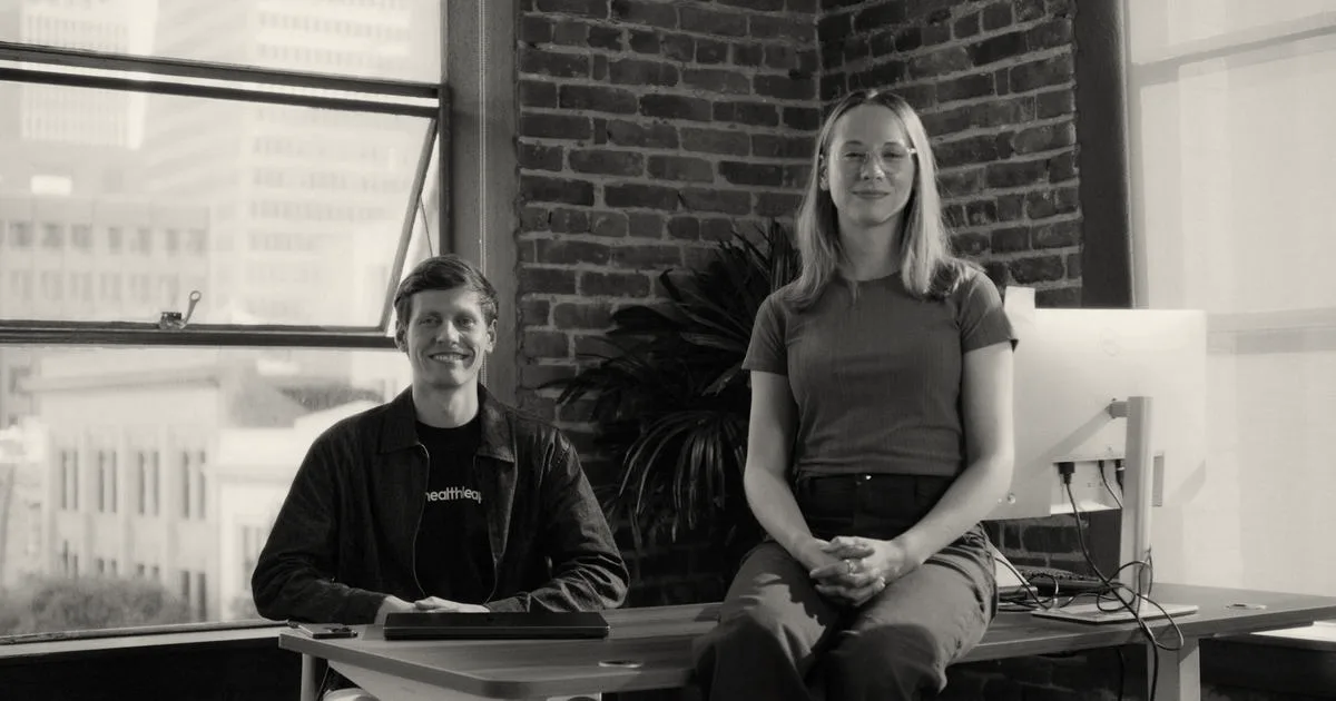 Healthleap co-founders Josiah and Jemima Meyer sitting at a desk in a brick-walled office.