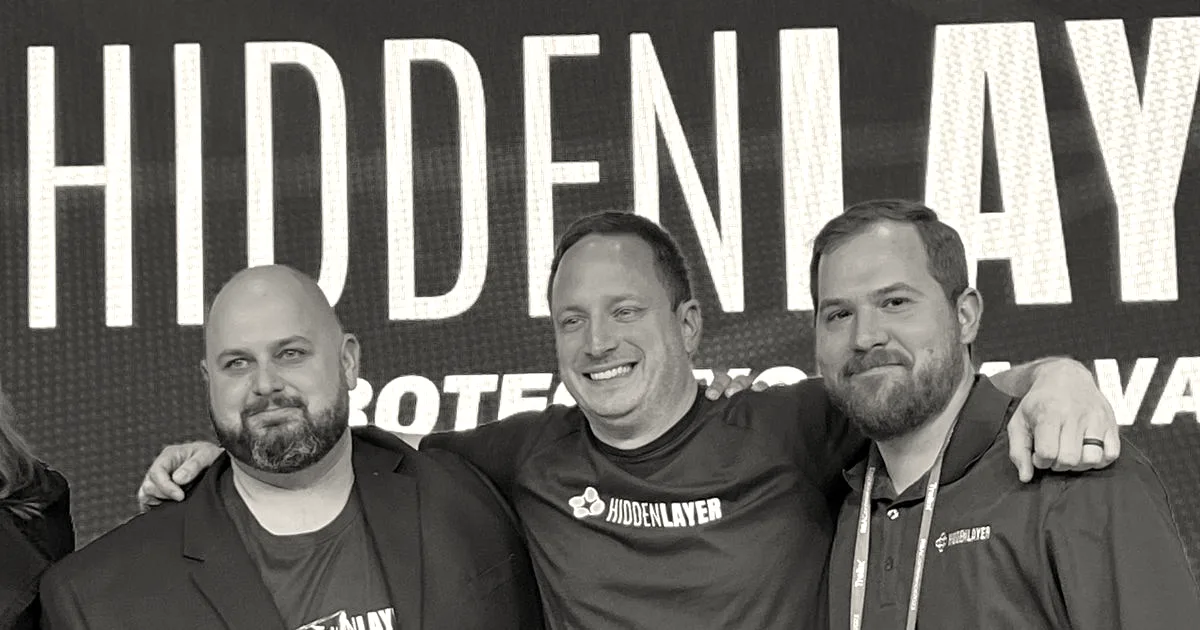Three men from HiddenLayer posing together with an award in front of a blue brand backdrop.