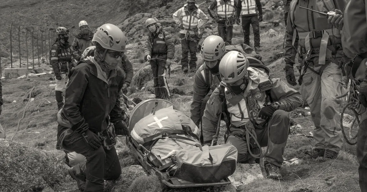 A mountain search and rescue team in helmets and gear attends to a hiker in an orange rescue stretcher.