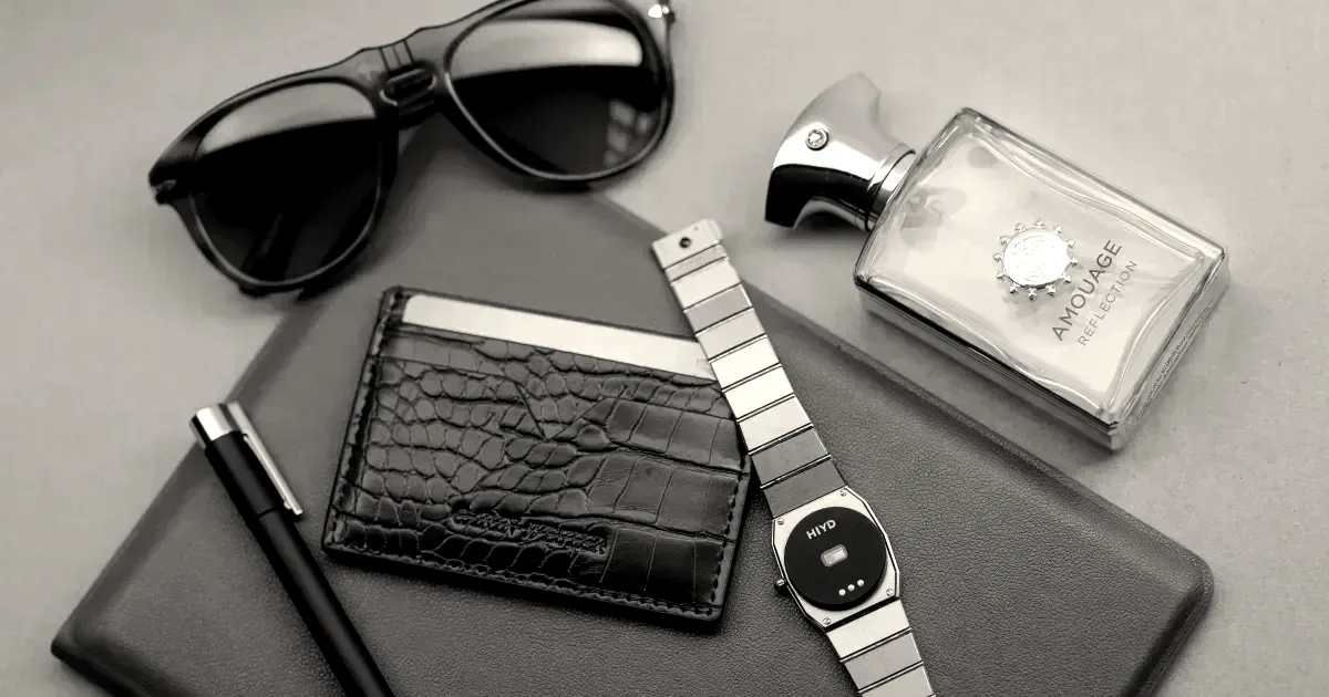 A wrist watch with a circular sensor attached to its underside resting next to a wallet and pen.