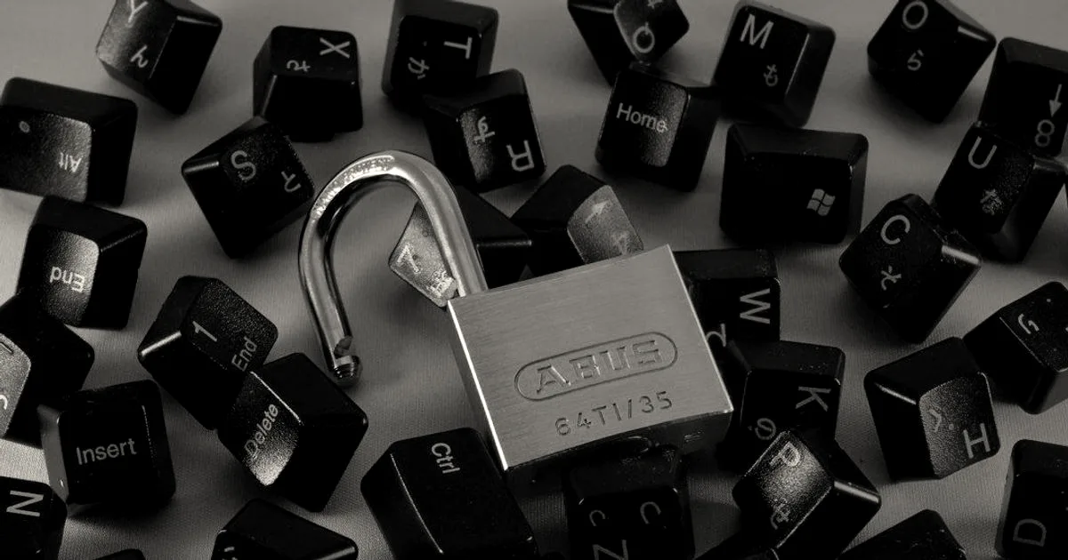 An open padlock resting among scattered black computer keyboard keys illuminated by red and green lighting
