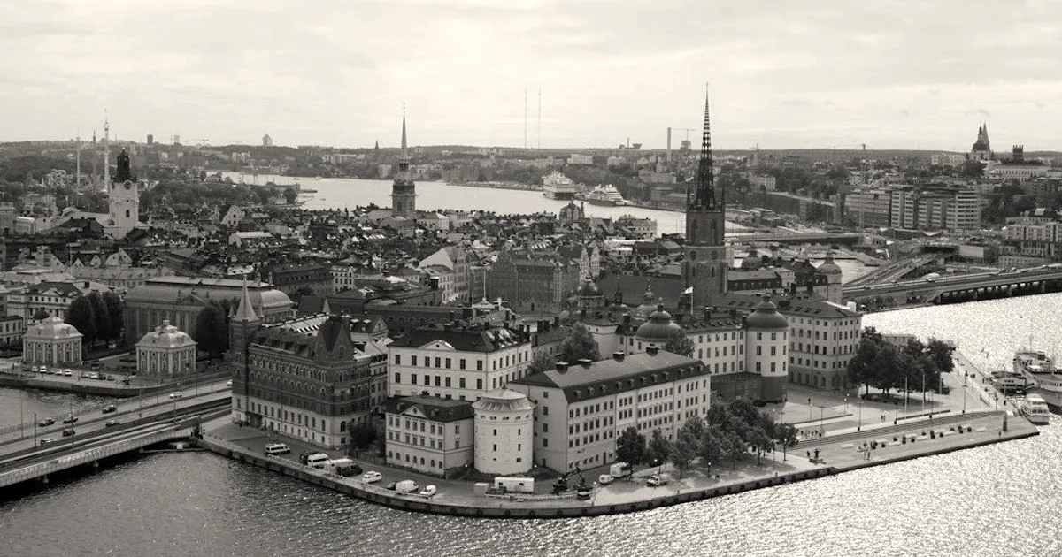 Aerial panoramic view of central Stockholm featuring Riddarholmen and Gamla Stan surrounded by waterways under a partly cloudy sky.