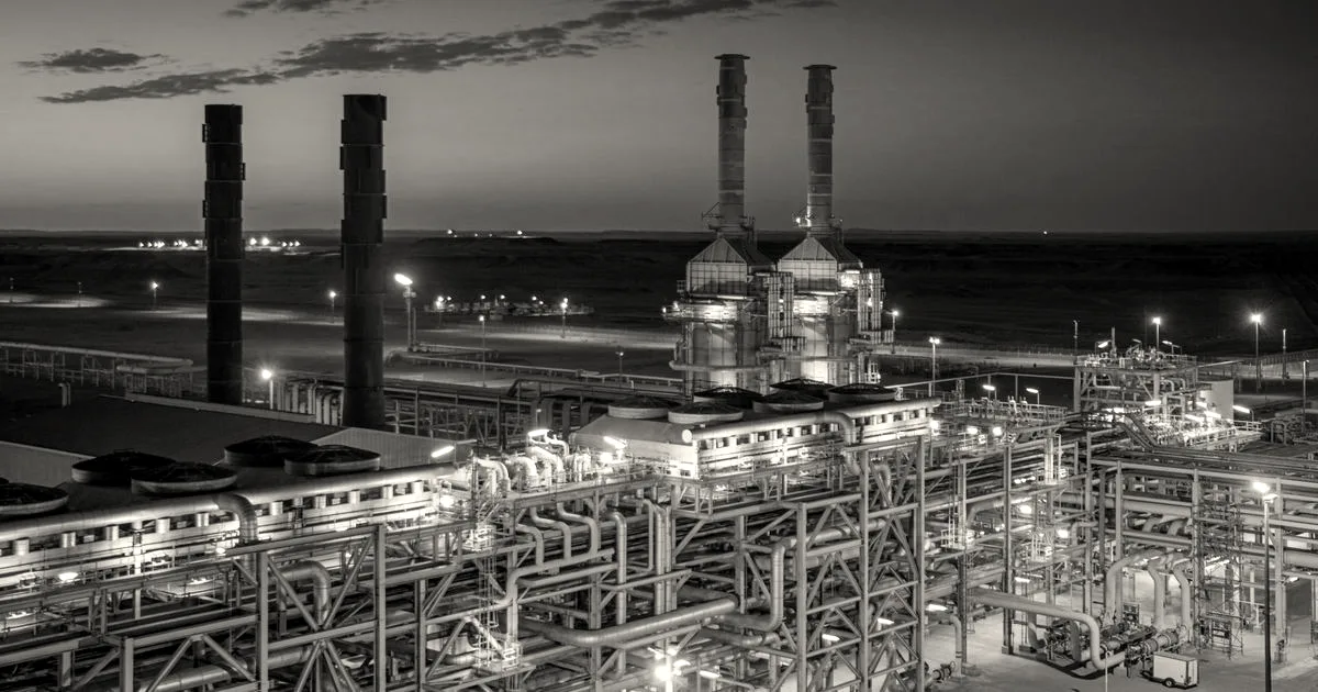 An illuminated industrial facility and power plant with tall chimneys set against a deep blue sunset sky.