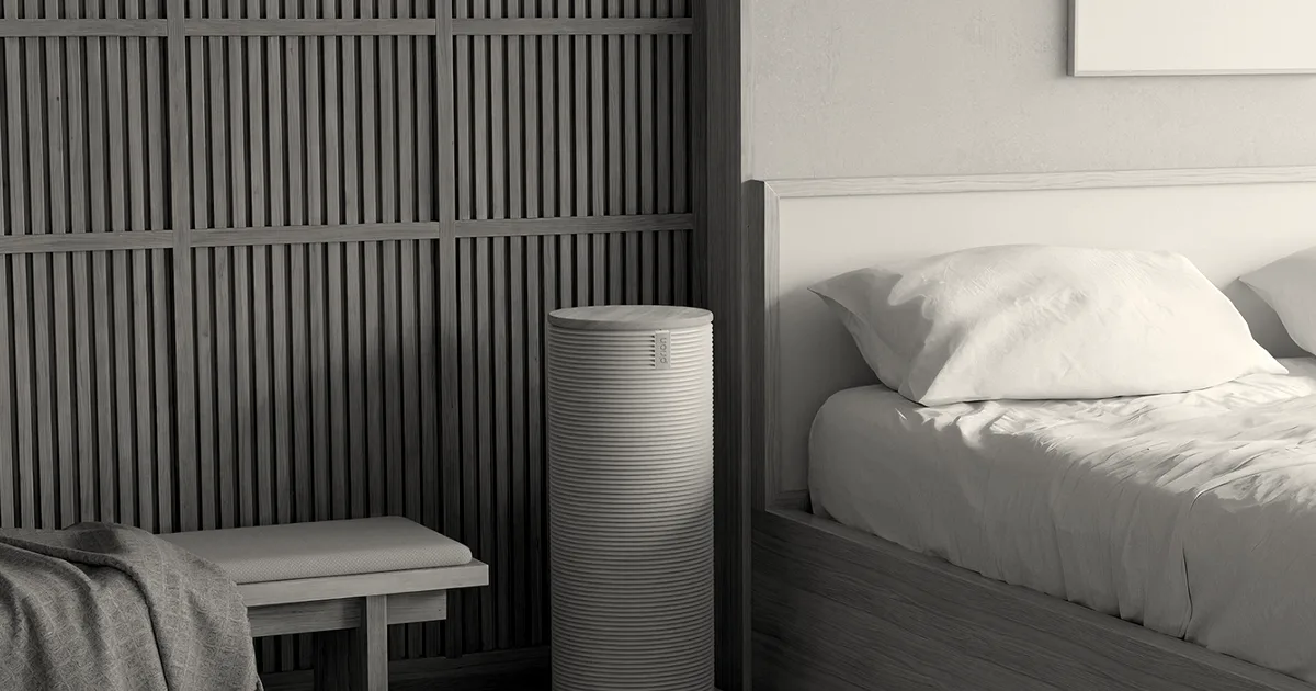 Cylindrical ribbed Orion device standing beside a wooden bed frame and bench in a bedroom