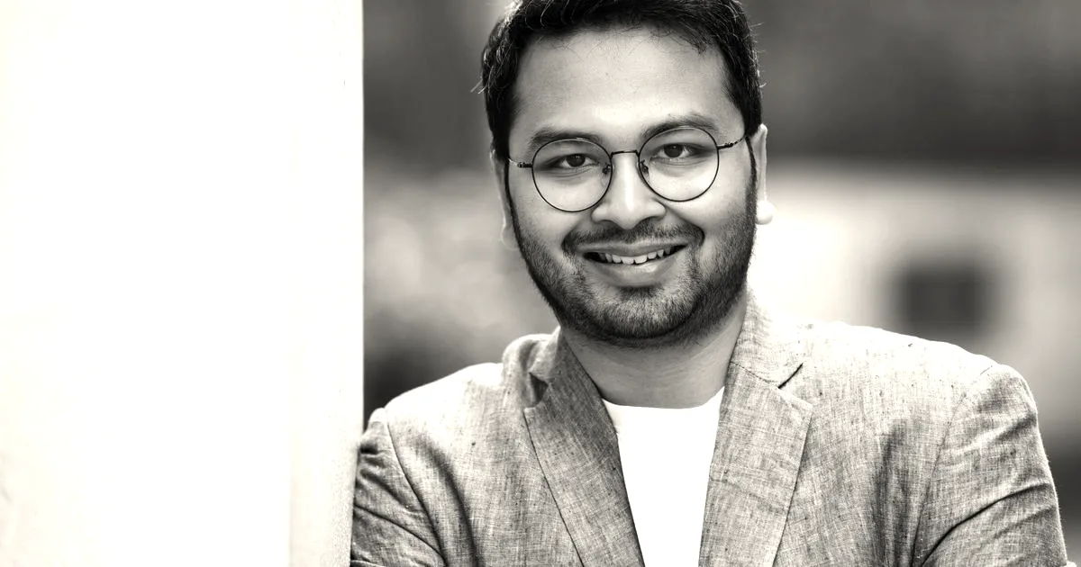 Portrait of Pocket FM founder Rohan Nayak smiling in a blue blazer and glasses.
