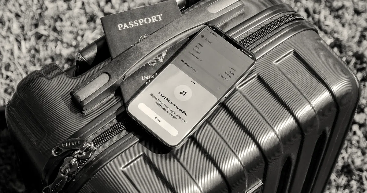 A smartphone showing an active mobile plan alongside a passport resting on a bright red suitcase outdoors.