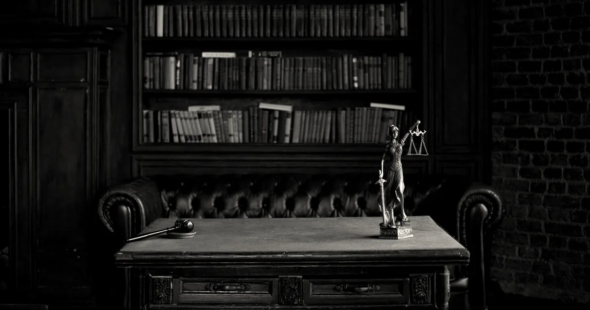 A classical study room featuring shelves of books, a wooden gavel, and a Lady Justice figurine on a table.