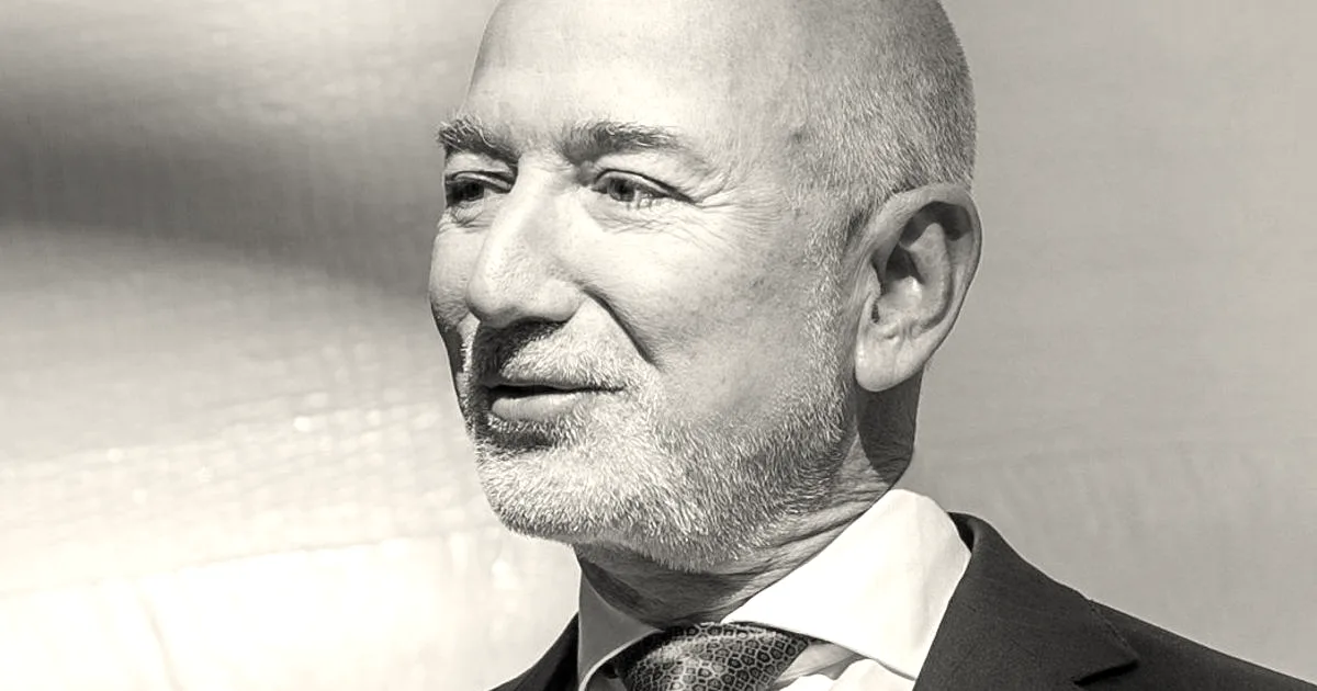 Close-up portrait of Jeff Bezos smiling in a dark suit with a red tie.