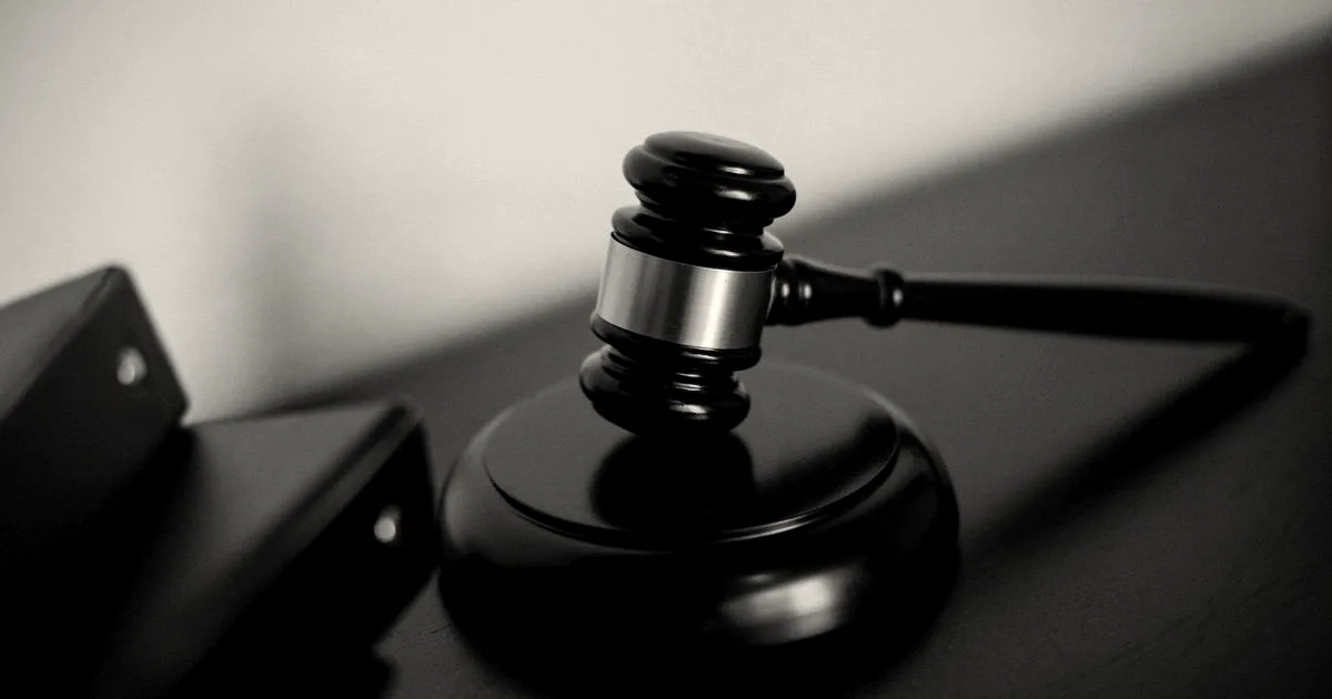 A dark wooden judge's gavel with a gold band resting on its sound block next to black folders.