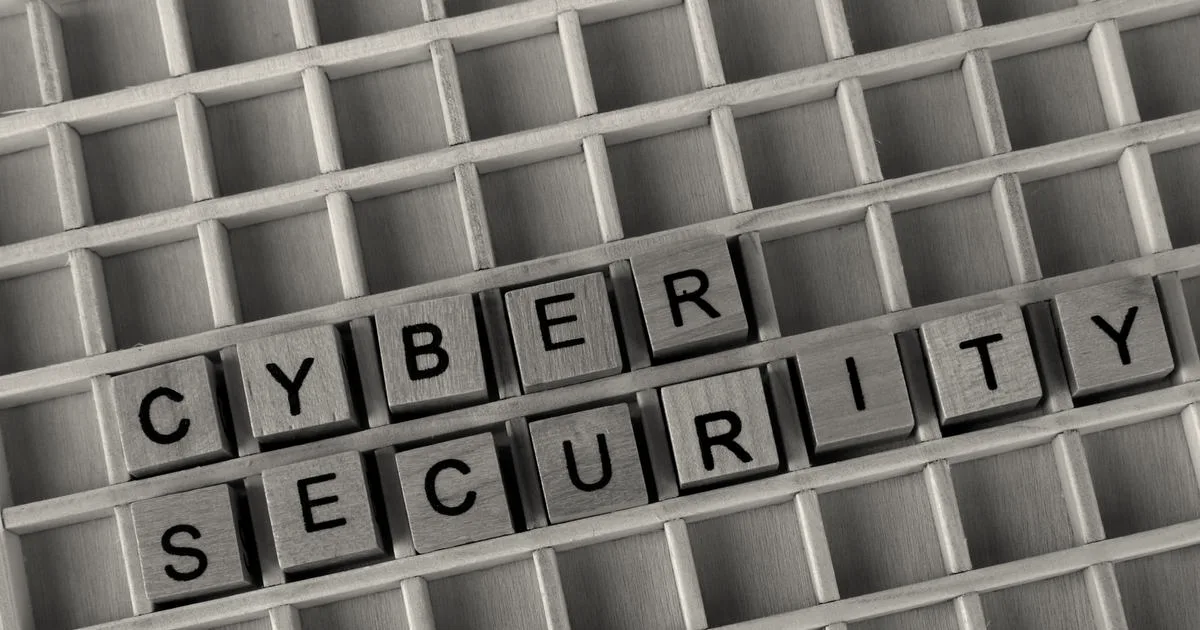 Wooden letter tiles spelling out 'CYBER SECURITY' arranged in a wooden grid tray.