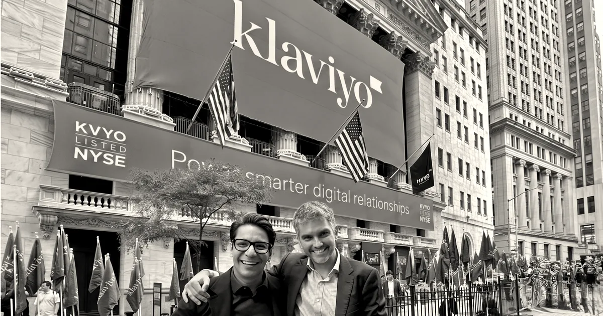 Two smiling men in suits standing outside the New York Stock Exchange under a Klaviyo banner.