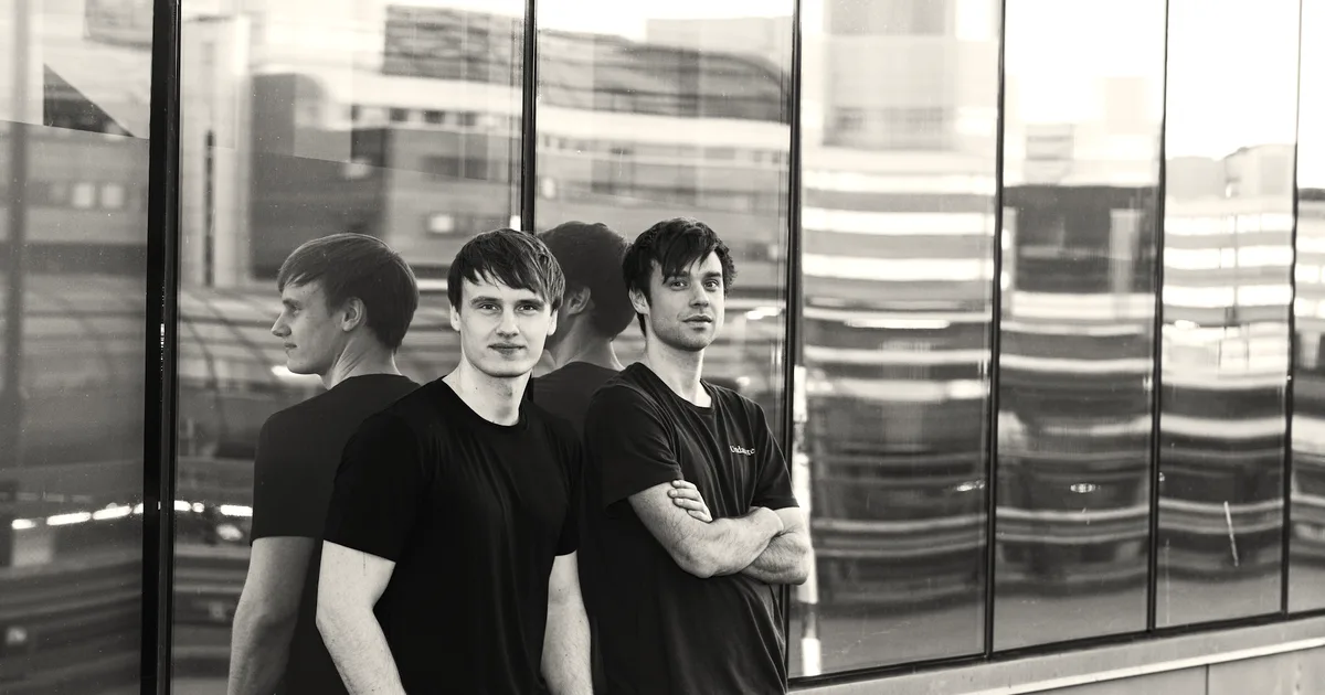 Two men standing together outdoors against a reflective glass building wall, representing Lovable's founders.