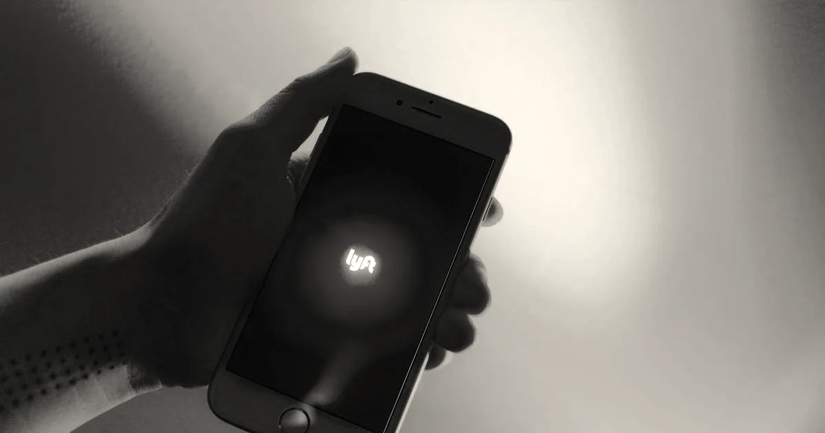 A hand holding a smartphone showing the Lyft logo on the screen against a vivid magenta background.