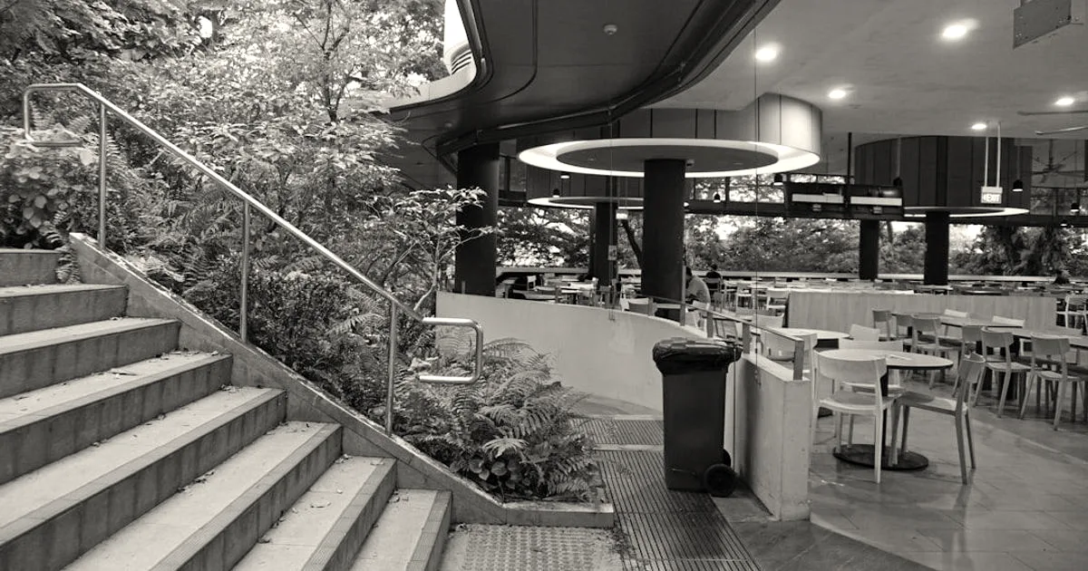 An outdoor dining area with tables and chairs alongside an open staircase surrounded by lush green trees.