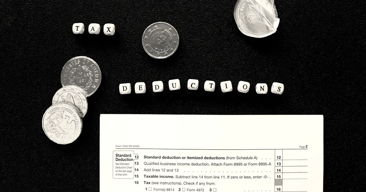 Coins, letter blocks spelling tax deductions, and a tax document arranged on a dark background.