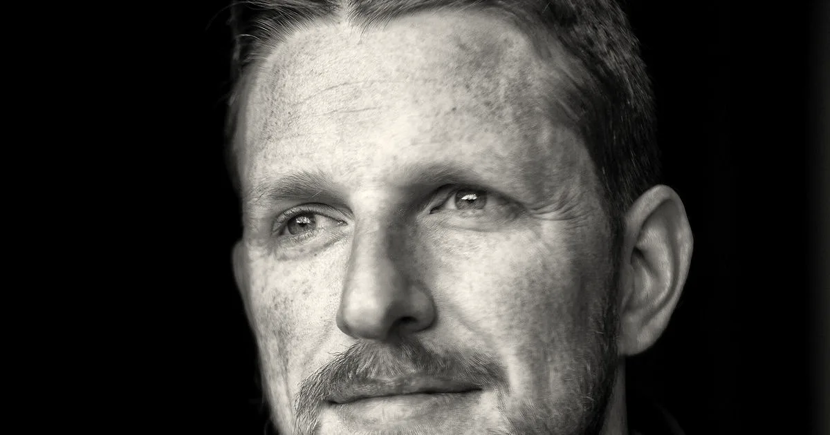 Black and white portrait photo of Matt Mullenweg smiling slightly against a dark background
