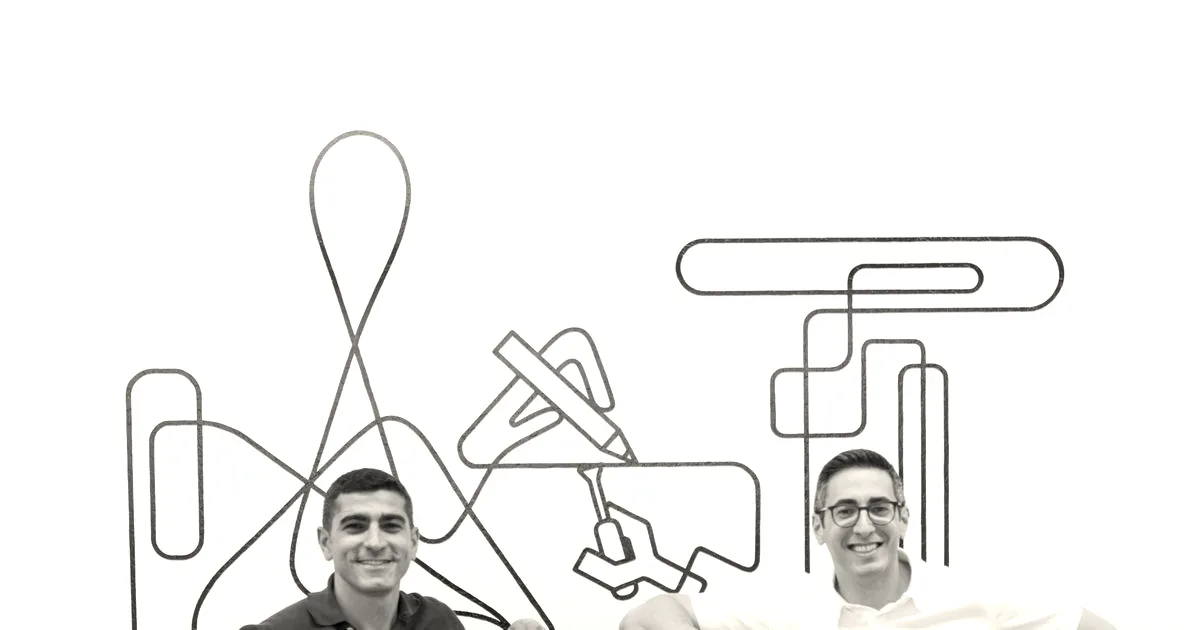 Two smiling co-founders standing alongside a mobile robotic arm in front of a white wall.