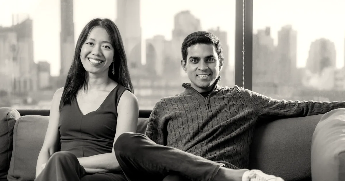 A man and woman smiling while sitting together on a modern sofa in an office with city view.