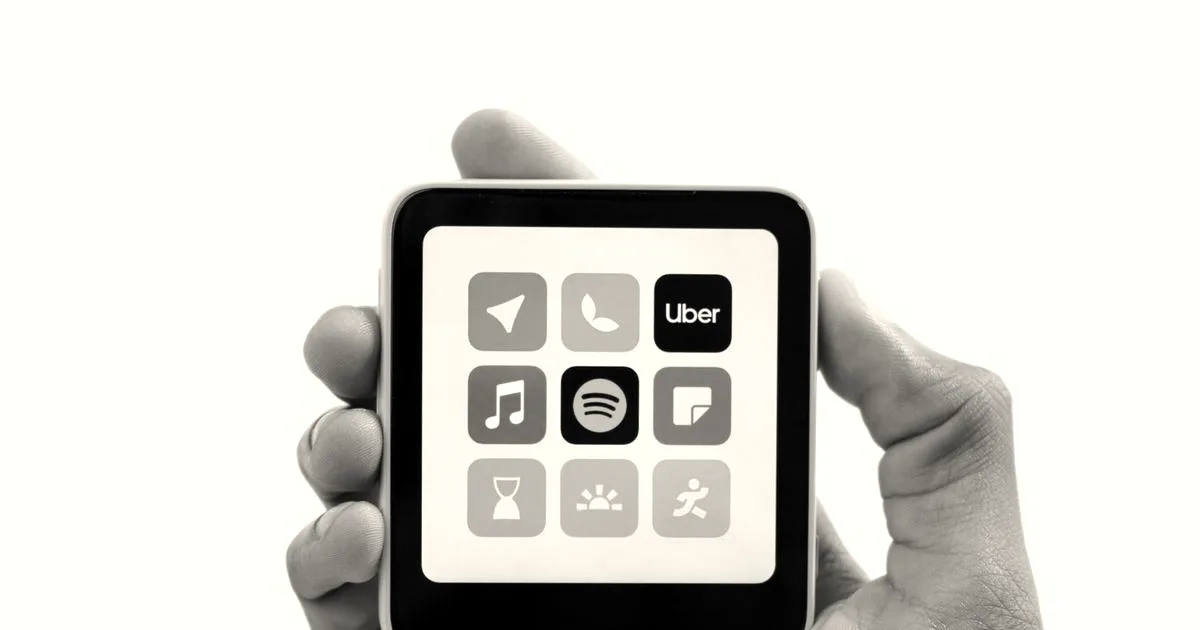 A person's hand holding a small square Meadow handheld device displaying minimalist app icons on its screen