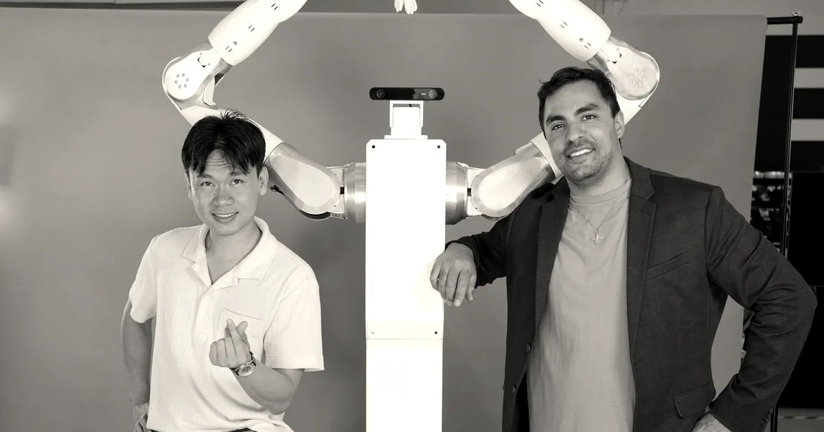 Feather Robotics co-founders pose alongside a tall white dual-armed robot forming a heart shape.