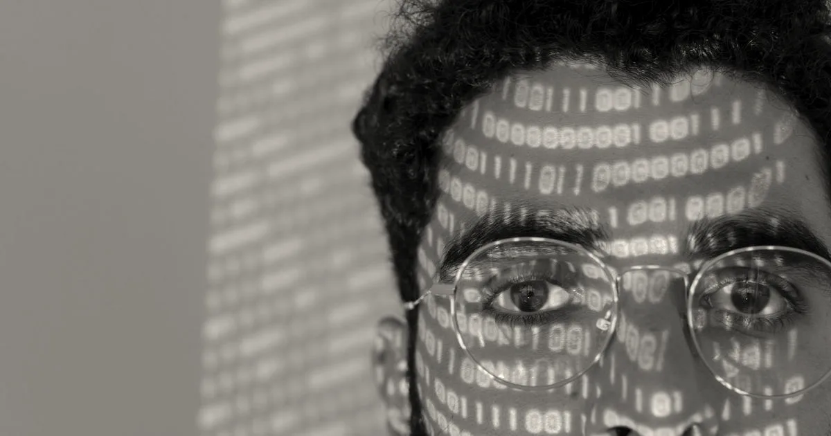 Close-up of a man's face with glowing green binary computer code projected across it.