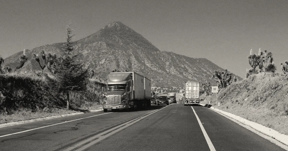 Semi trucks driving down an open highway with a large mountain peak under a clear blue sky