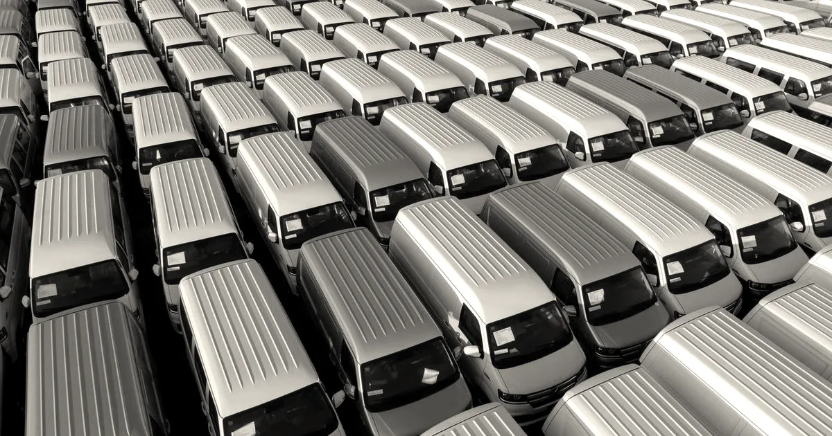 Aerial view of rows of white fleet vans parked neatly together in a large parking lot.