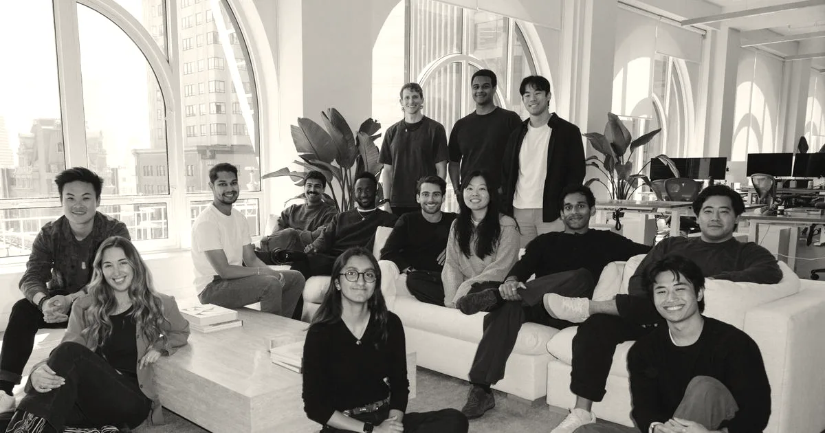 A group of thirteen diverse team members posing together in a bright, modern office space.