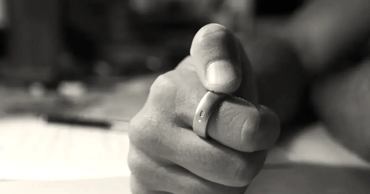 A close-up shot of a person wearing a sleek silver Natura smart ring on their index finger.
