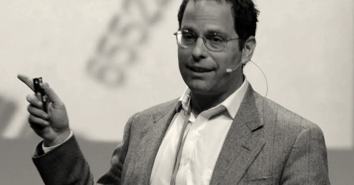 Portrait of Neil Rimer speaking at a conference, wearing glasses and a tweed jacket with a microphone.