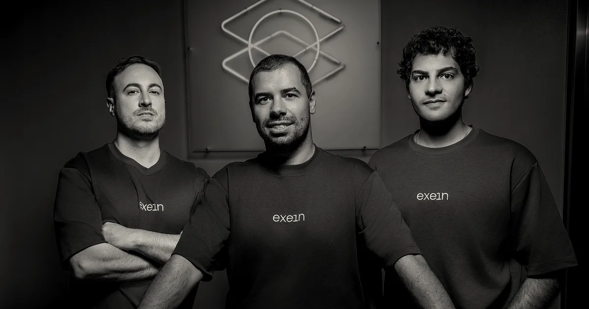 Three Exein founders standing together against a blue background wearing matching dark green branded t-shirts.
