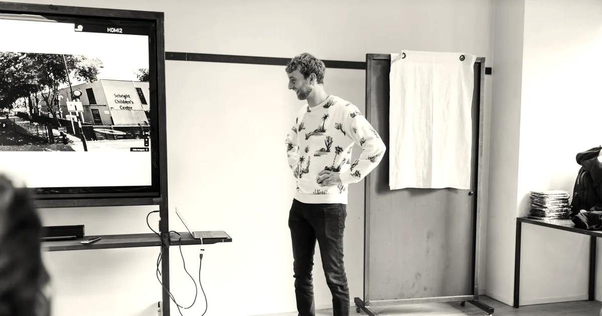 Man presenting on a large screen in a modern office setting, engaging an audience.