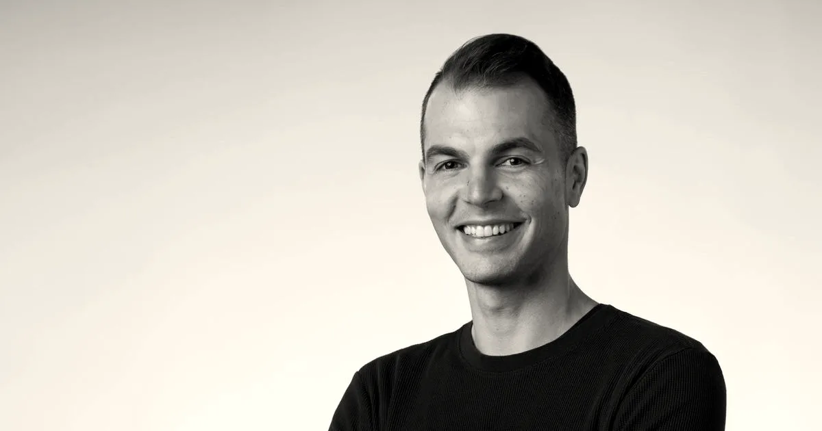 Portrait of smiling Nvidia executive Adel El Hallak with folded arms against a grey background.