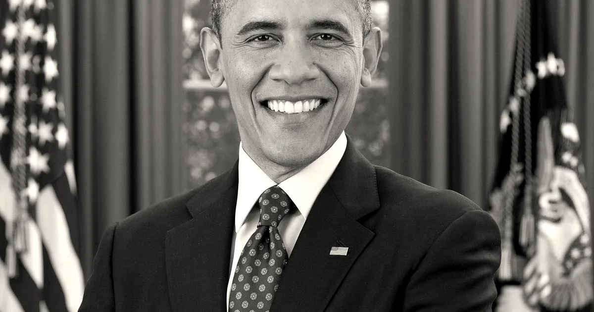 Official portrait of Barack Obama smiling with arms crossed in front of American flags.
