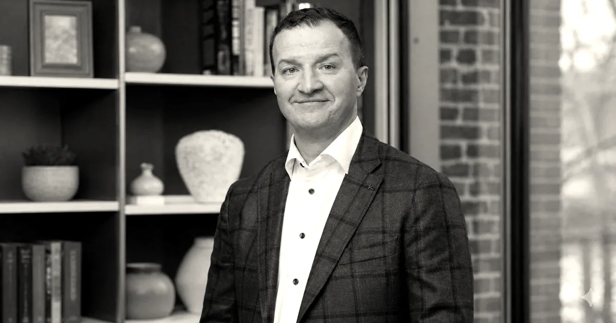 Portrait of Dali Rajic wearing a blue patterned blazer and white shirt in front of a bookshelf.