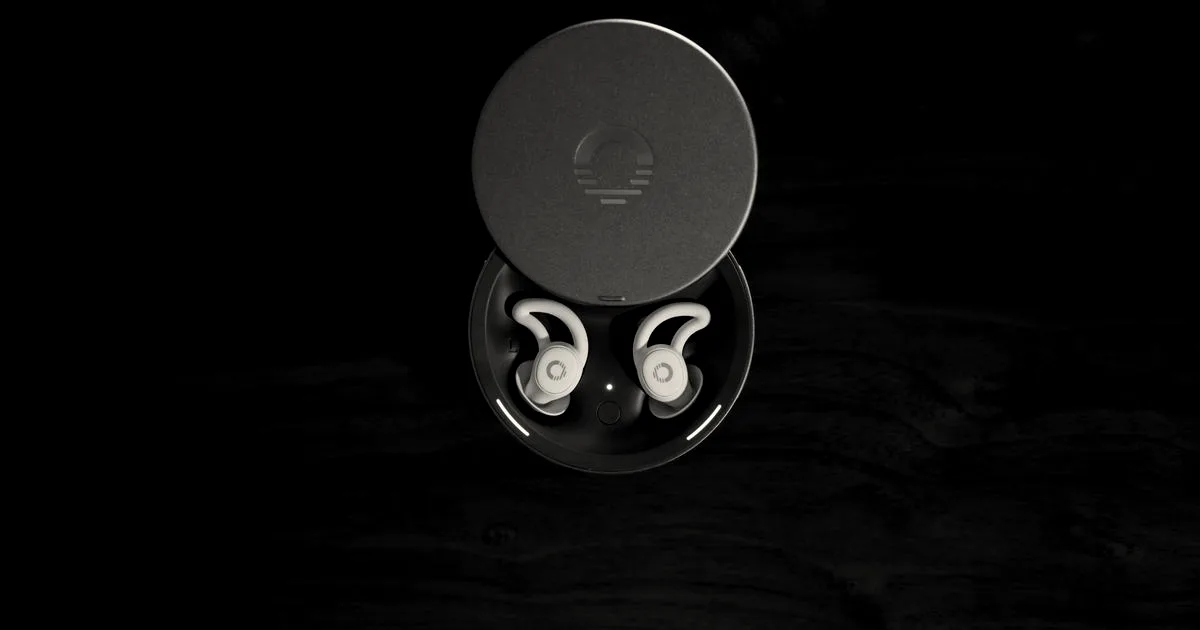 Ozlo sleepbuds case and earbuds shown from above on a dark wooden surface in low lighting.