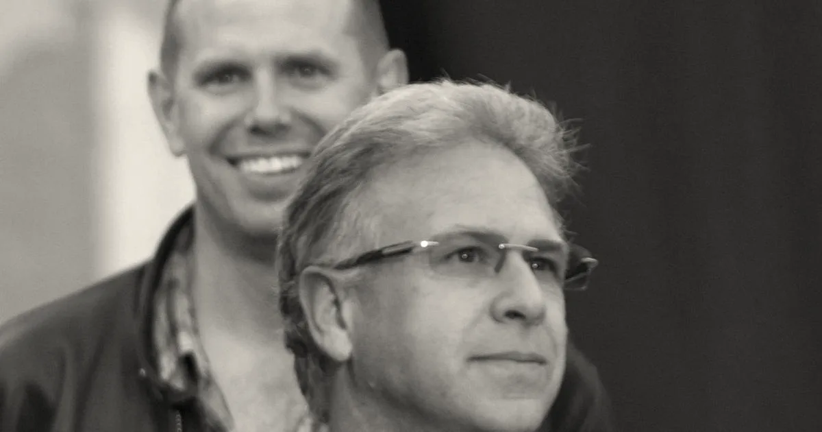 Phil Schiller wearing glasses and a blue polo shirt holding a professional camera.