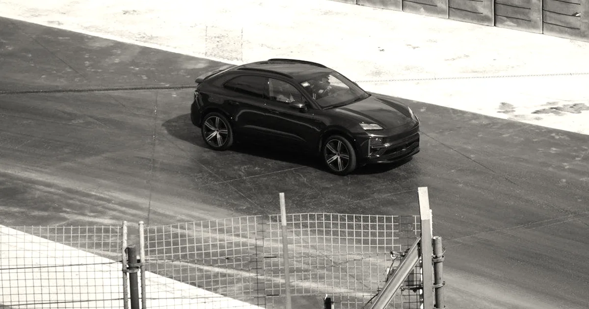 A dark green Porsche Macan Electric driving along an asphalt track with protective barrier walls.