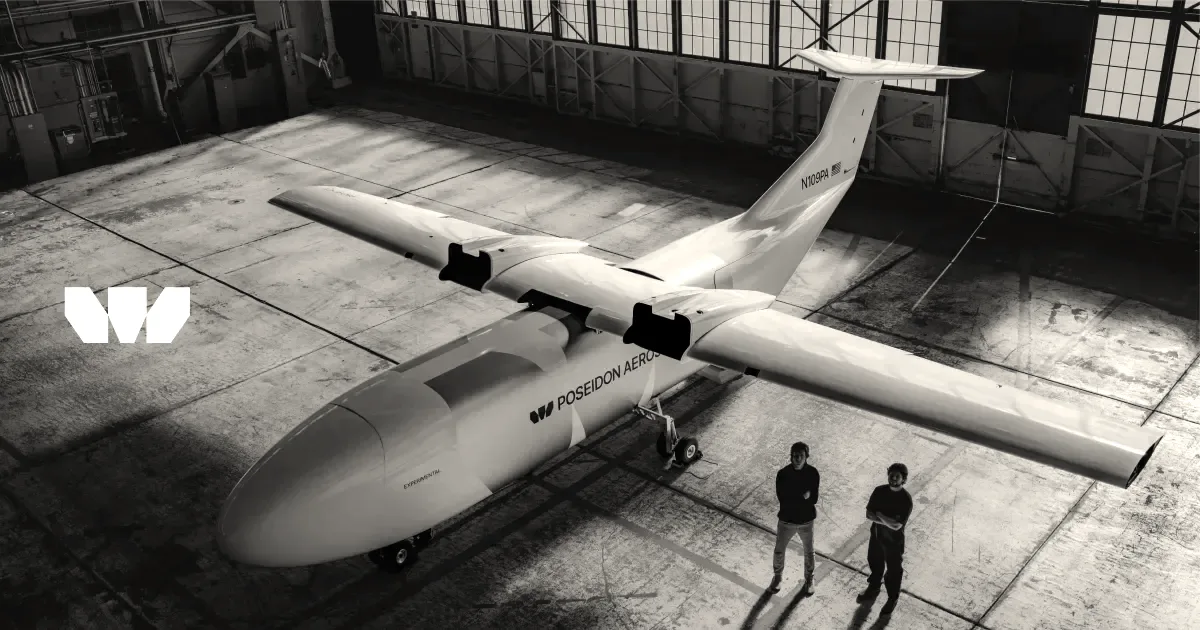 A white Poseidon Aerospace pilotless cargo aircraft in a hangar with two team members standing alongside.