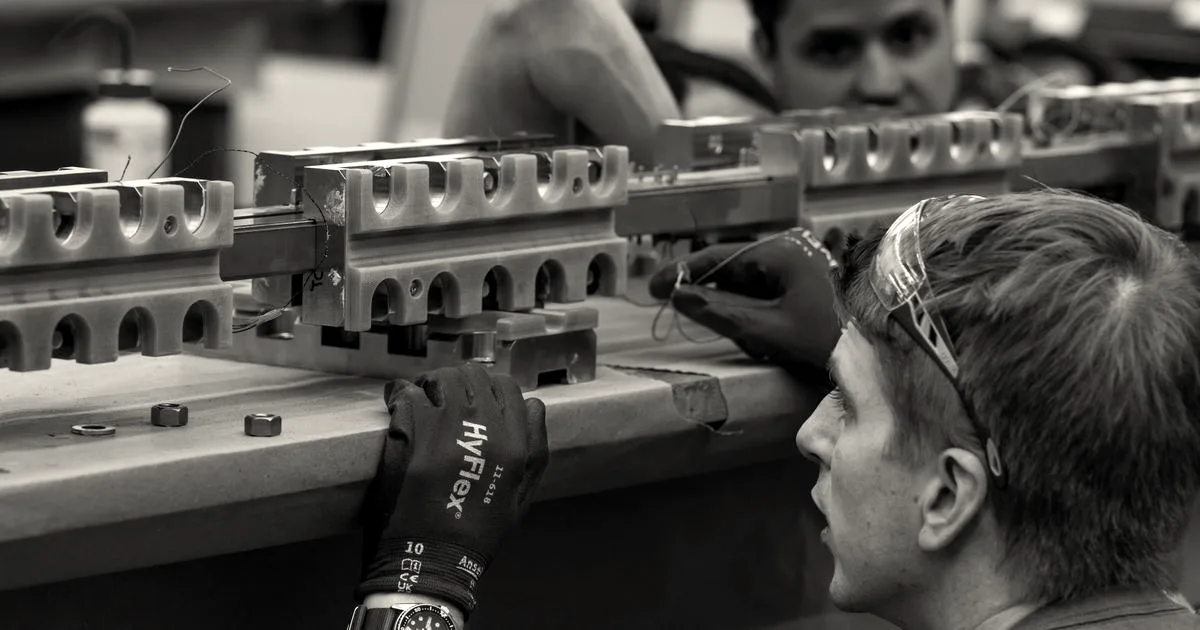 An engineer wearing protective glasses and blue work gloves inspects a precision fusion reactor component.