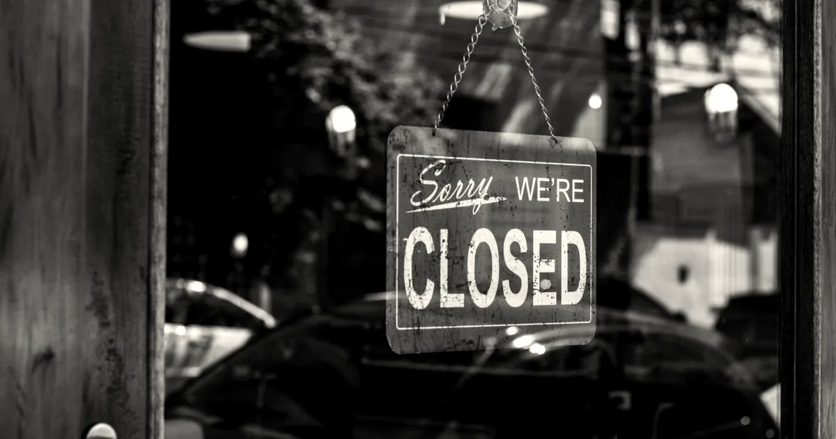 A red rectangular sign hanging on a glass door with white text reading Sorry WE'RE CLOSED.