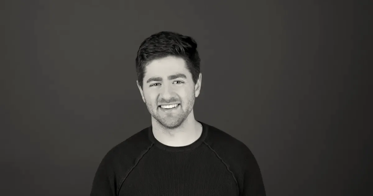 Portrait of Ramp CEO Eric Glyman smiling against a plain dark grey background.