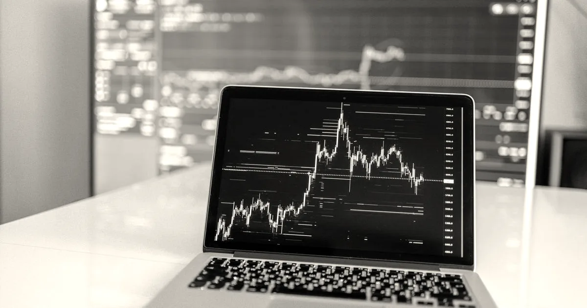 Laptop displaying cryptocurrency trading chart on a white desk.
