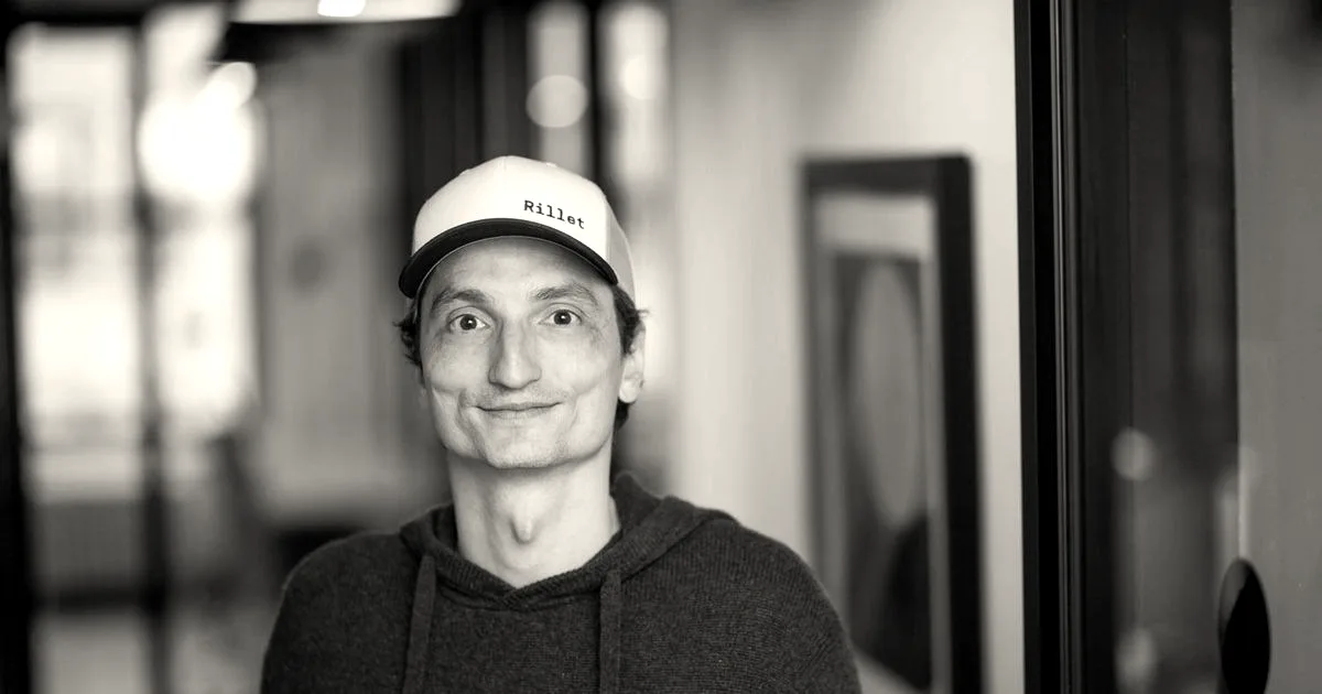 Portrait of Nicolas Kopp, founder and CEO of Rillet, wearing a blue hoodie and white cap indoors.