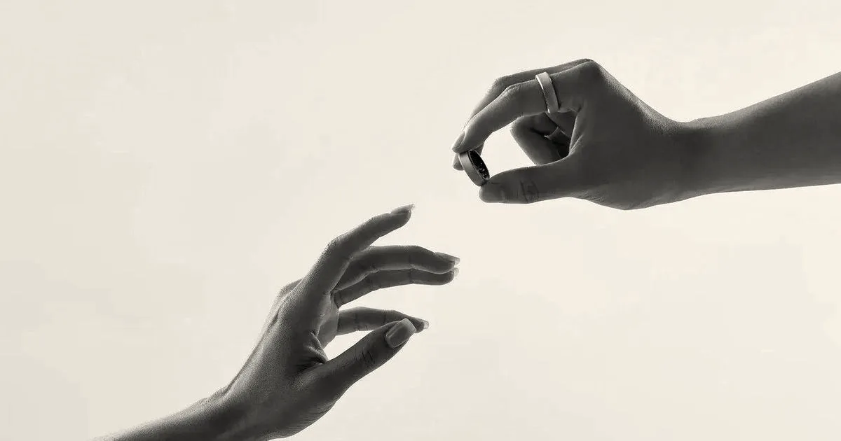 Two hands reaching toward each other with one holding a small smart ring.