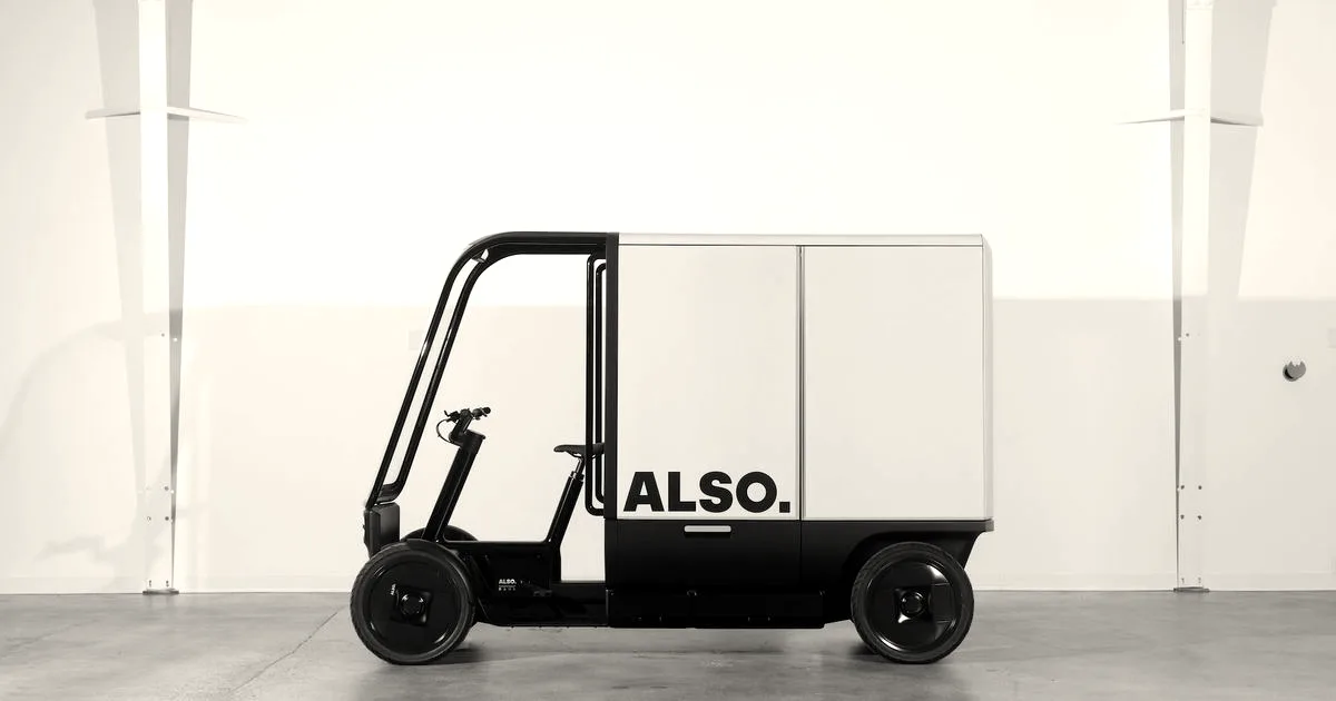 A sleek white and black Also electric delivery quad vehicle parked in a bright studio warehouse.