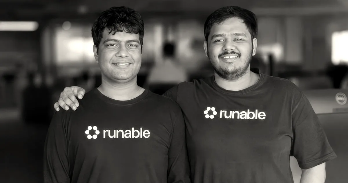 Two smiling men, the co-founders of Runable, standing side by side wearing matching black t-shirts with the Runable logo.