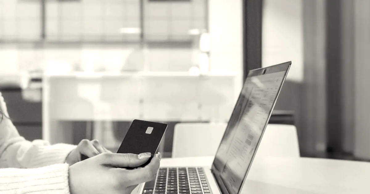 A person holding a sleek black payment card in front of an open laptop on an office desk