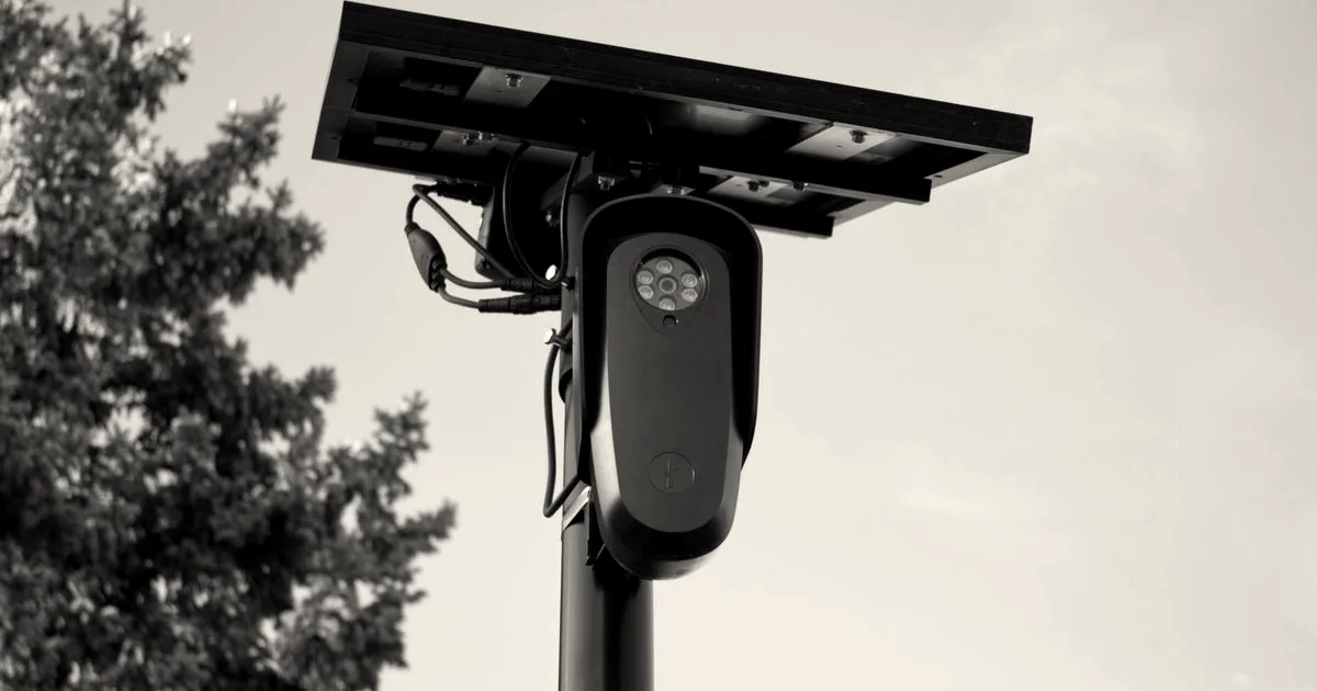 A solar-powered automated license plate reader camera mounted on a pole against a blue sky