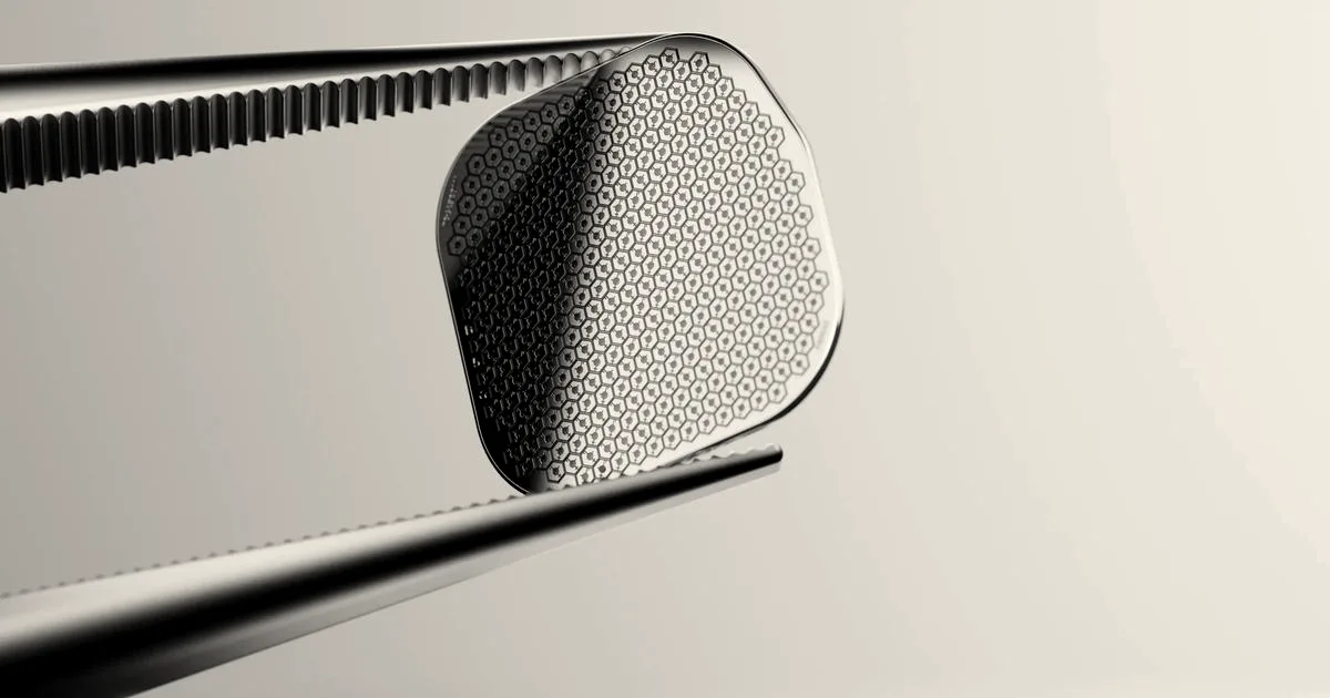 Close-up of tweezers holding a tiny microchip above specialized vision-restoring glasses.